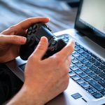 Pessoa jogando em notebook gamer com controle nas mãos