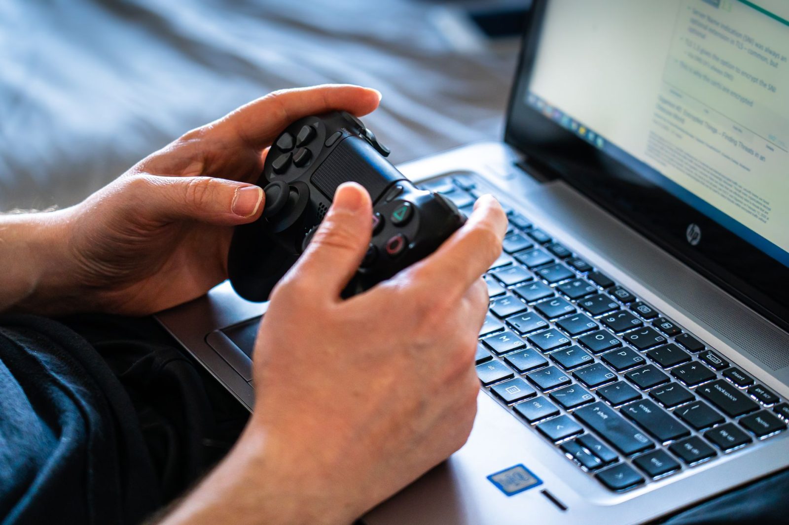 Pessoa jogando em notebook gamer com controle nas mãos
