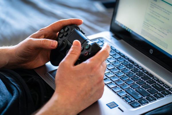 Pessoa jogando em notebook gamer com controle nas mãos