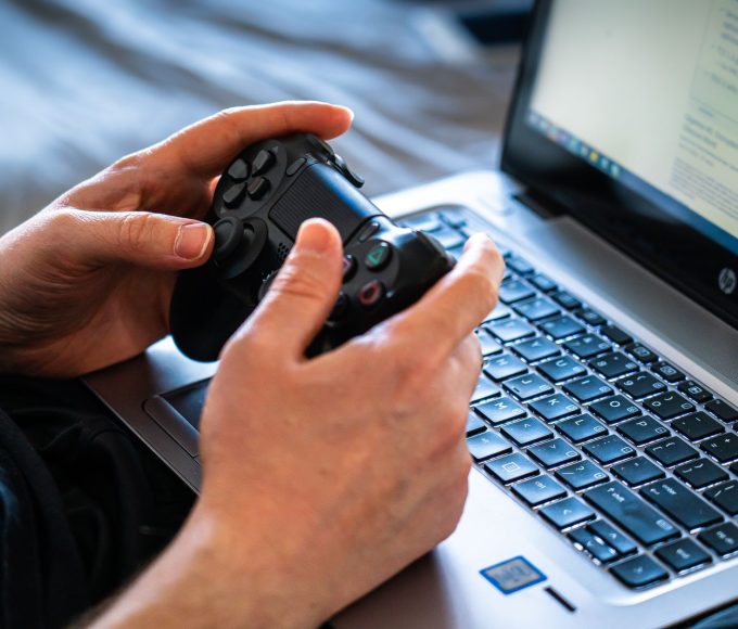 Pessoa jogando em notebook gamer com controle nas mãos